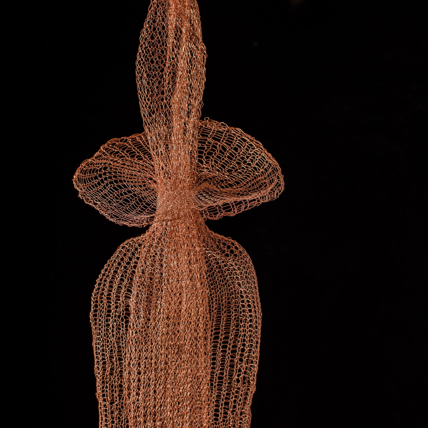 Artistic representation of a human figure made from interwoven copper wire on a black background