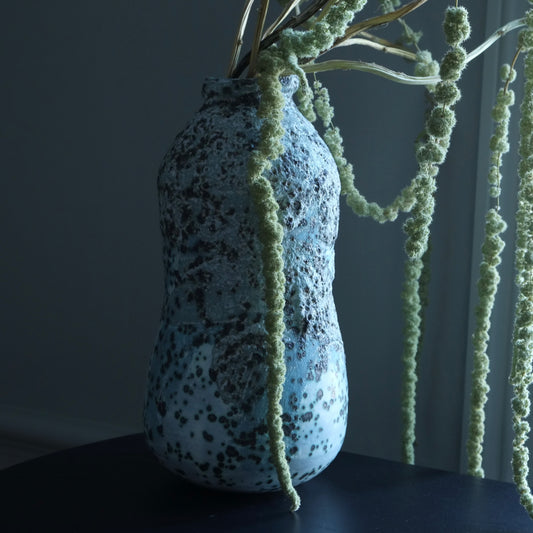 Speckled blue vase with plant against a dark background