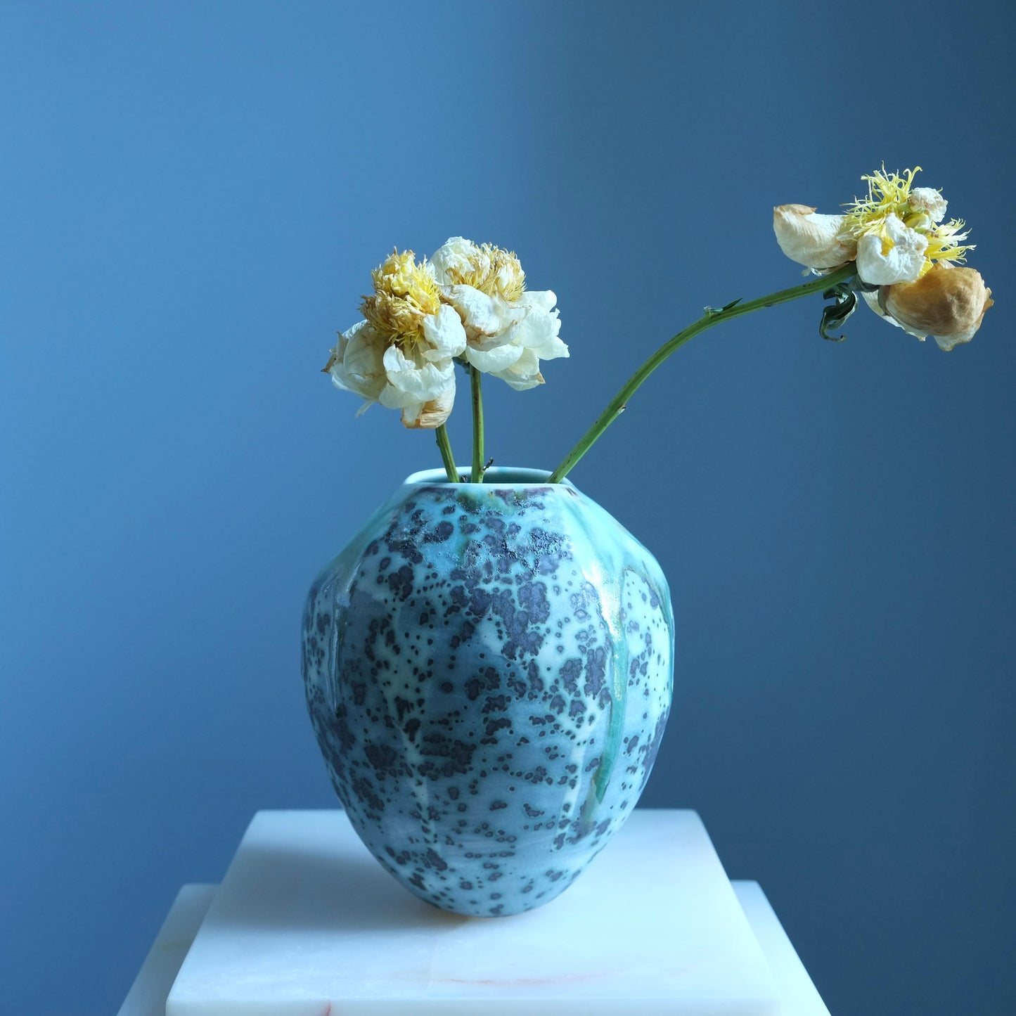 Speckled blue vase on a white pedestal against a blue background