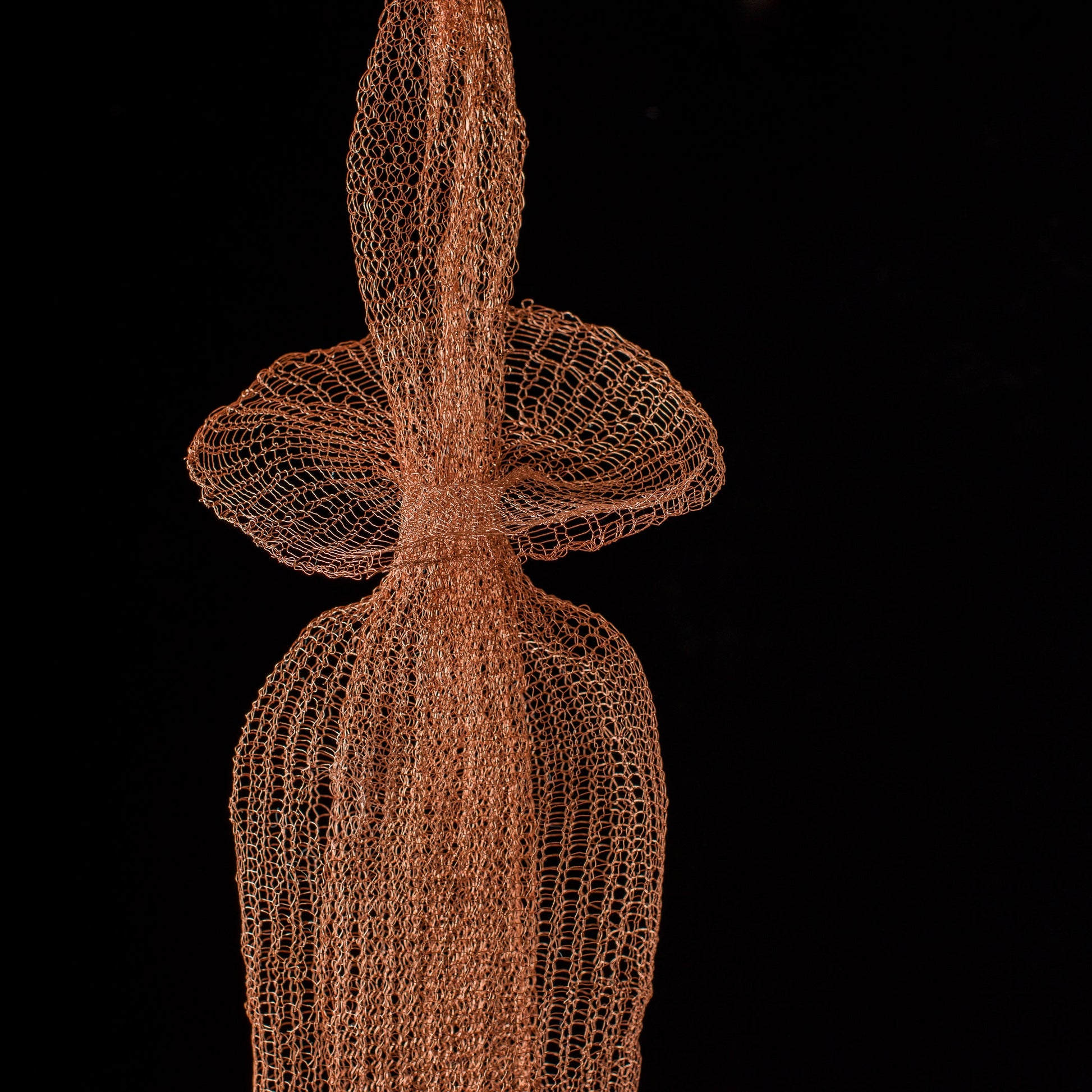 Artistic representation of a human figure made from interwoven copper wire on a black background