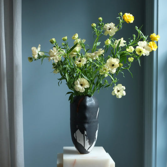 Bouquet of flowers in a black and white vase against a blue wall
