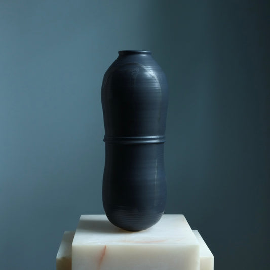 Black vase on a white pedestal against a dark background