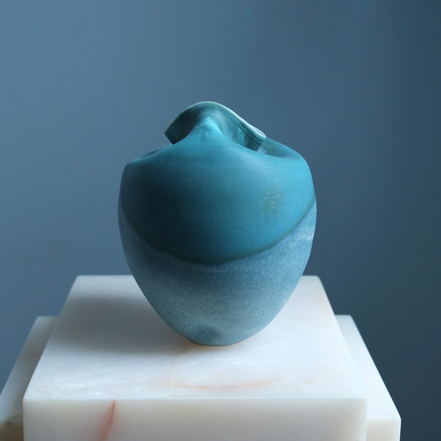 Blue ceramic sculpture on a white pedestal against a gray background