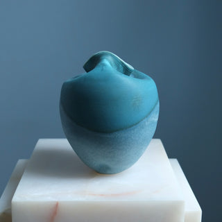 Blue ceramic sculpture on a white pedestal against a gray background