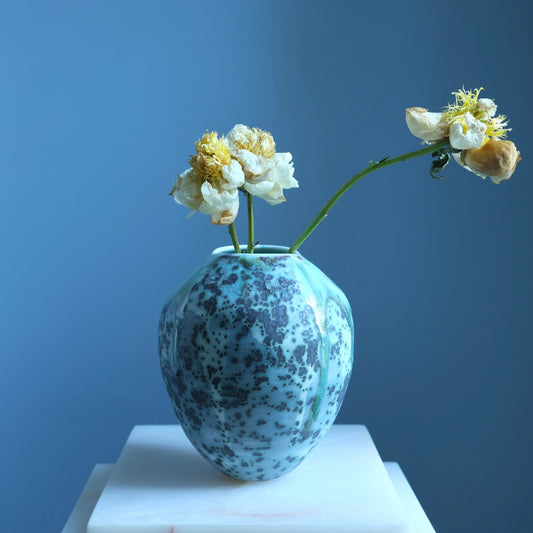 Speckled blue vase  on a white pedestal against a blue background