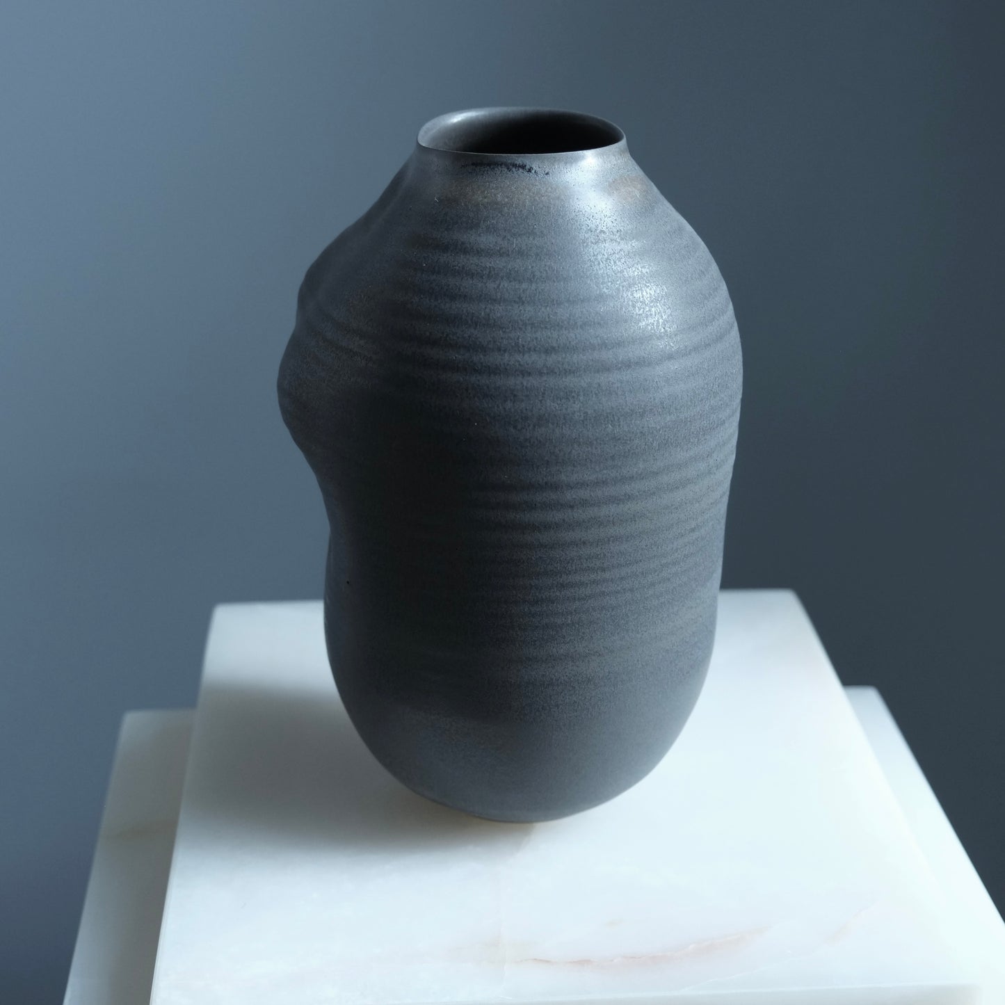 black textured vase on a white surface with a gray background