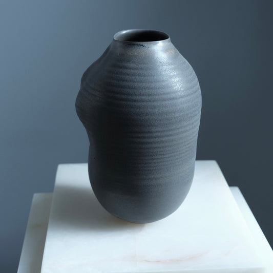 black textured vase on a white surface with a gray background