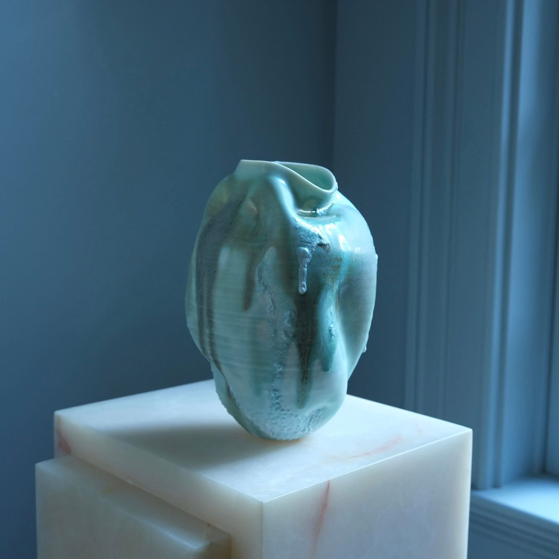 Textured green ceramic vase on a white pedestal against a blue wall.