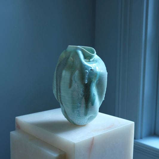 Textured green ceramic vase on a white pedestal against a blue wall.