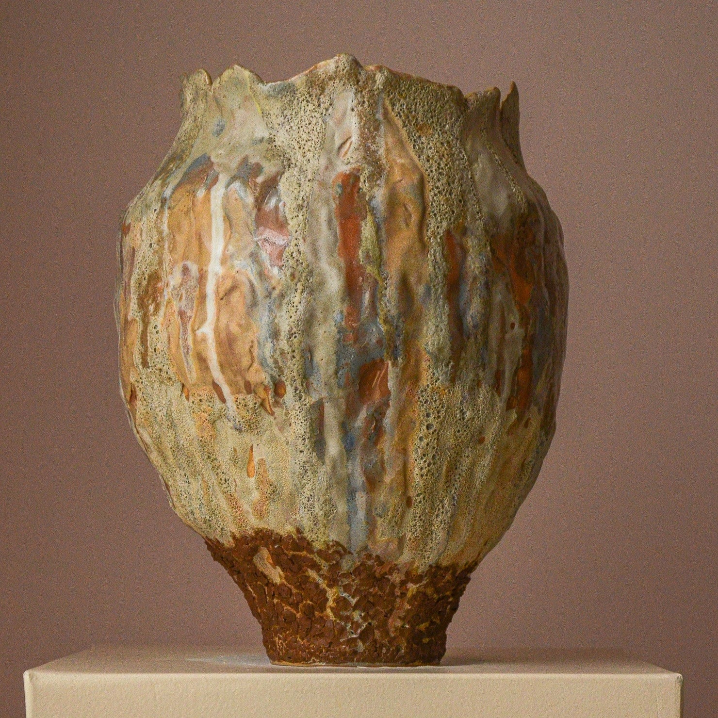 Rustic ceramic vase with textured surface on a beige pedestal against a brown background