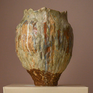 Rustic ceramic vase with textured surface on a beige pedestal against a brown background