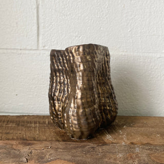 Textured bronze vase on a wooden surface by Sarah Mijares Fick